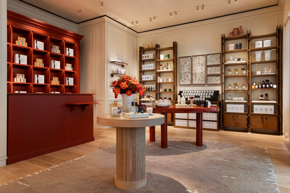 A boutique interior in one of Nashville's charming retail spots features decorative shelves displaying perfumes and candles. A round table with flower arrangements sits elegantly on a beige rug, while cream walls and warm lighting create a cozy ambiance.