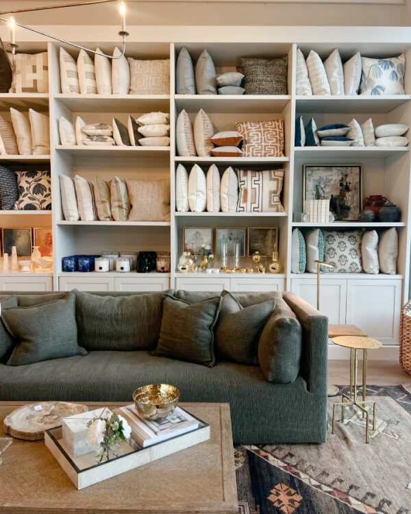 Cozy living room display with a gray sofa, patterned pillows on shelves, and various decorative items. A wooden coffee table with a small plant and bowl is in the foreground, inviting you to explore this Nashville-inspired retail haven.