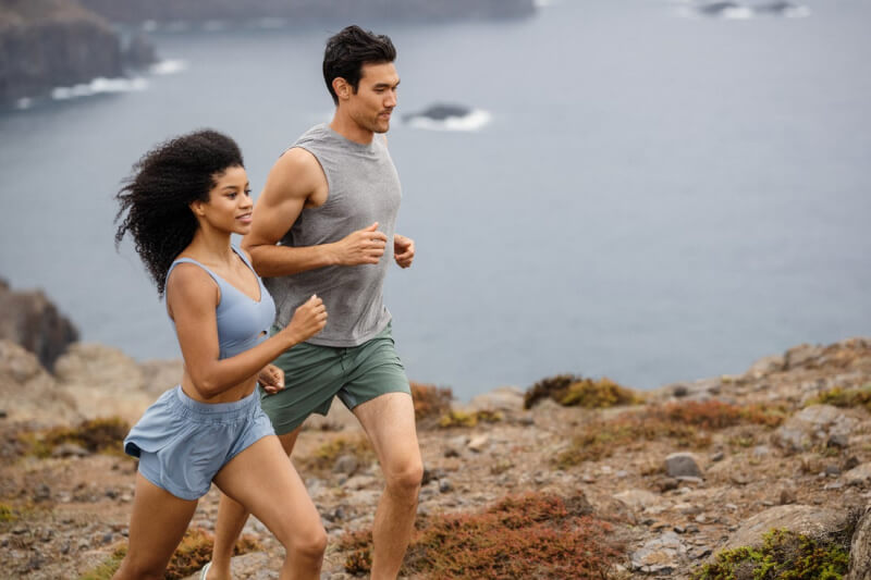 Two people are exploring a rocky coastal path, jogging with the ocean as their backdrop. Clad in athletic clothing, they embrace the invigorating sea breeze on their scenic adventure.