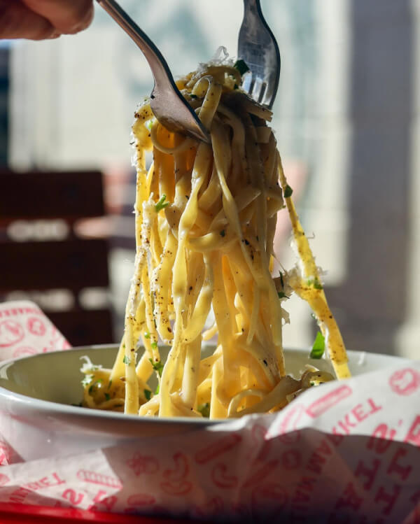9 New Nashville Restaurants to Try This Month - 22 A bowl of fettuccine pasta is lifted by a fork and spoon, garnished with herbs and grated cheese, in natural daylight.