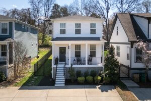 A charming two-story white house at 2509A Solon Dr, Nashville, TN, features a welcoming front porch with black chairs. It boasts a neatly landscaped yard and is surrounded by similar style homes, complete with a paved driveway in front.