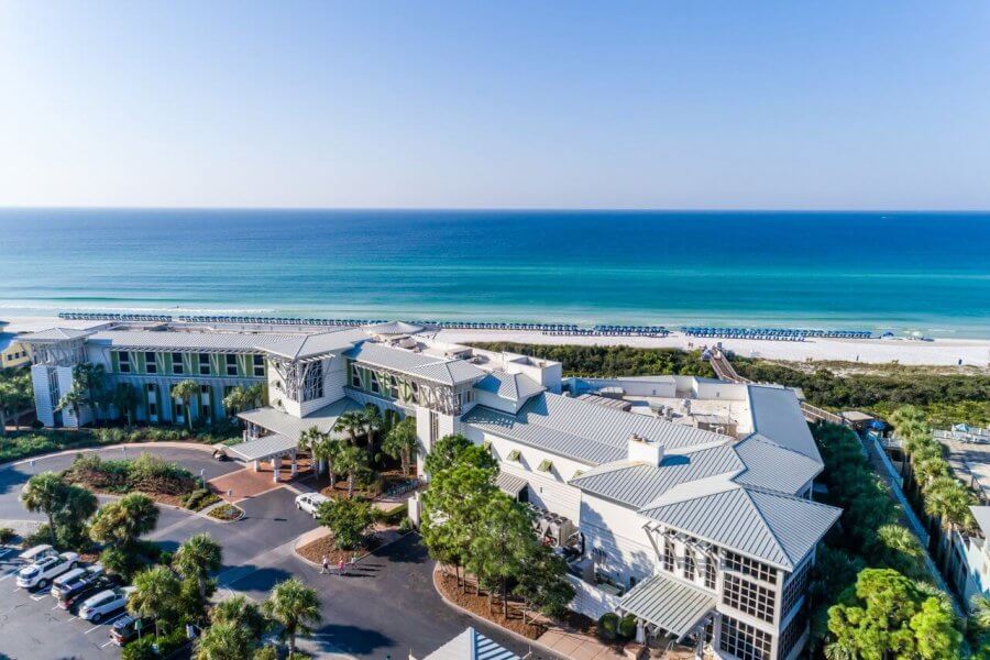 5 Reasons South Walton is Becoming the Premier Destination for Corporate Events and Meetings - 1 Aerial view of a large beachfront building with a parking lot, green landscaping, and a boardwalk leading to a sandy beach and blue ocean—an ideal venue for your next event in South Walton.