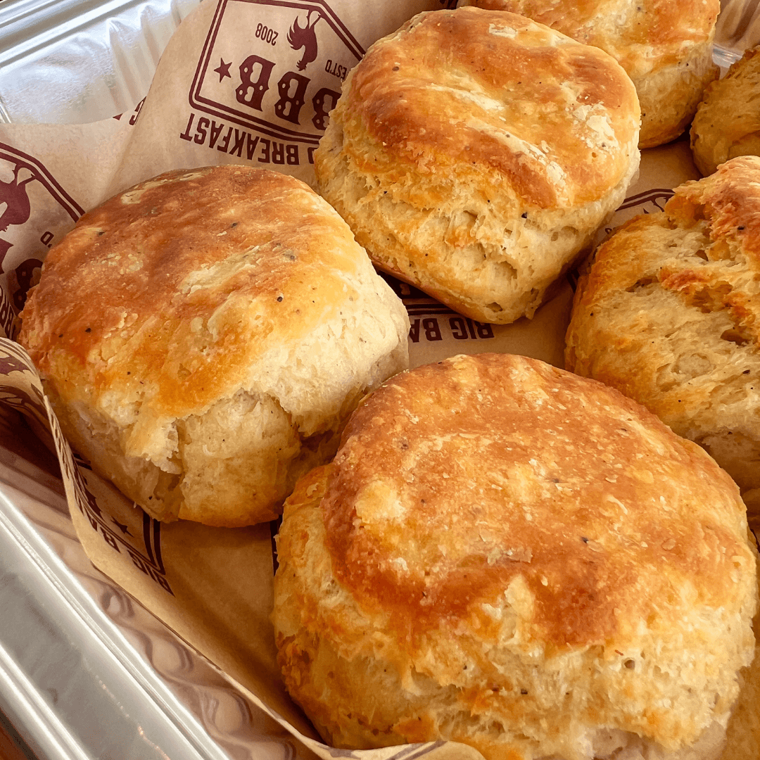 Big Bad Breakfast Returns to 30A. And Itâs as Delicious as You Remember. - 1 Golden, fluffy biscuits arranged on branded parchment paper in a metal trayâperfect for a delicious breakfast at Big Bad Breakfast.