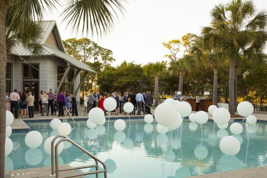 5 Reasons South Walton is Becoming the Premier Destination for Corporate Events and Meetings - 5 A group of people gather near a building and bar at an outdoor pool decorated with large white balloons and surrounded by palm trees during an event in South Walton.