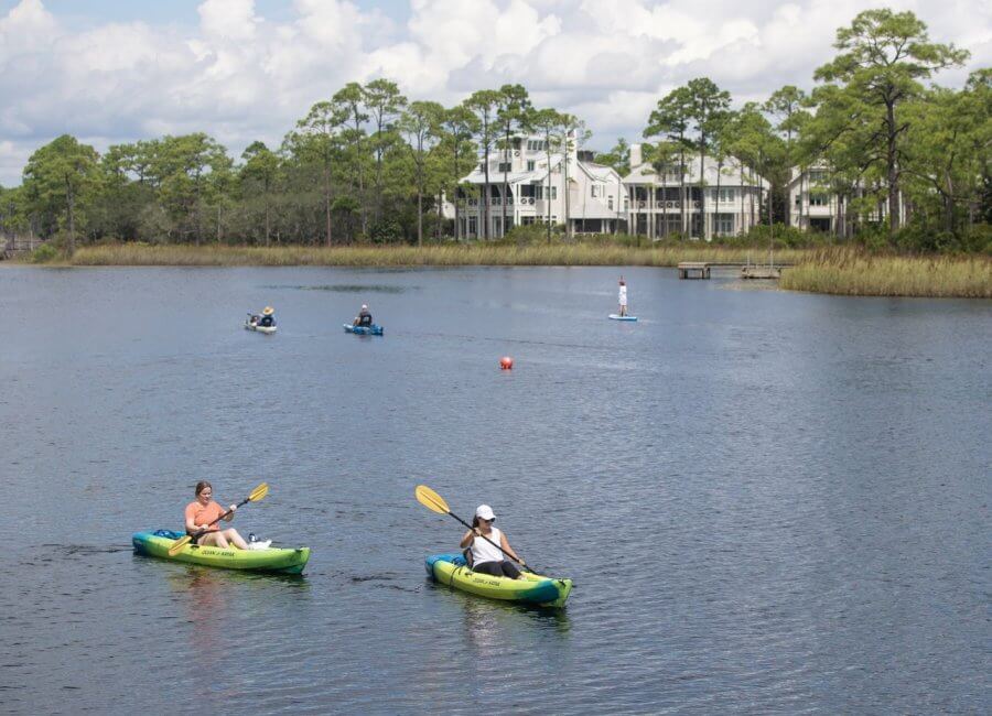 5 Reasons South Walton is Becoming the Premier Destination for Corporate Events and Meetings - 9 Two people kayaking on a lake with others canoeing and paddleboarding in the background during an event in South Walton; houses and trees line the shore under a partly cloudy sky.