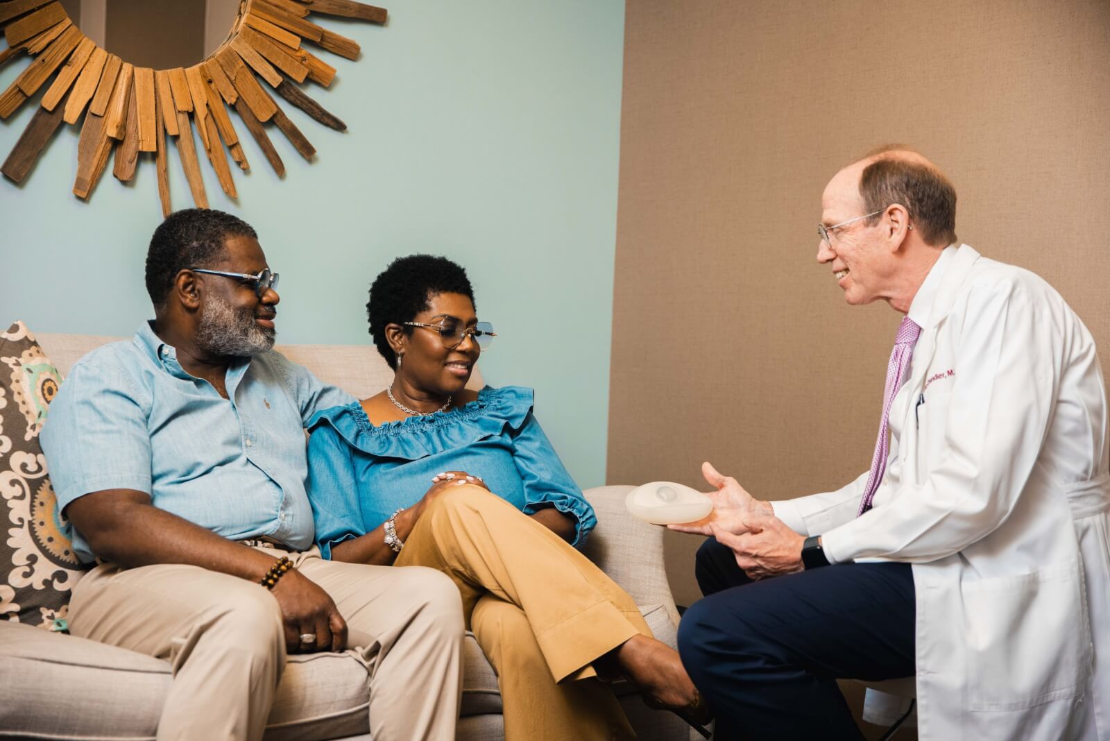 A doctor in a white coat from Surgery Group discusses a medical implant with a seated couple in an office setting in Memphis.
