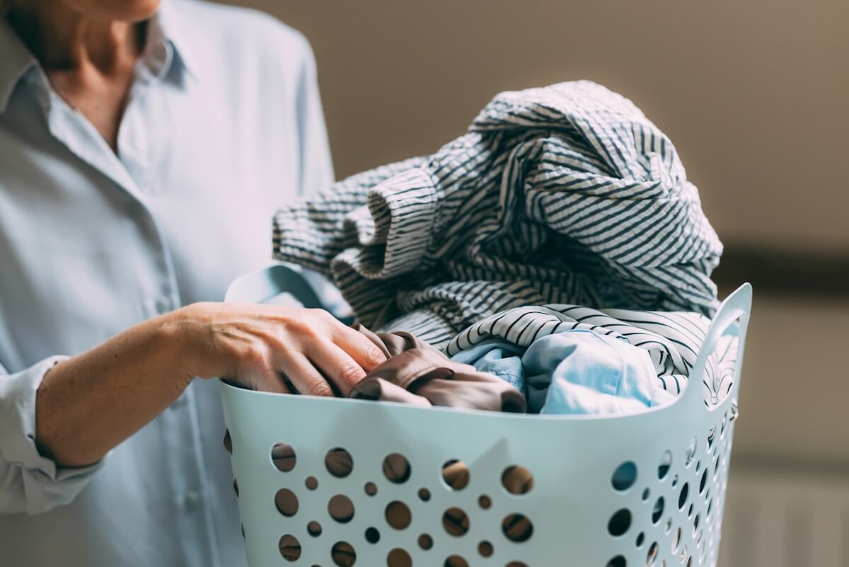 Shocking Stats About Microplastics You Need to Know (Seriously.) - 2 A person holding a light blue laundry basket filled with assorted clothes, including striped and solid-colored items—a reminder of the shocking stats on microplastics shed from fabrics during every wash.