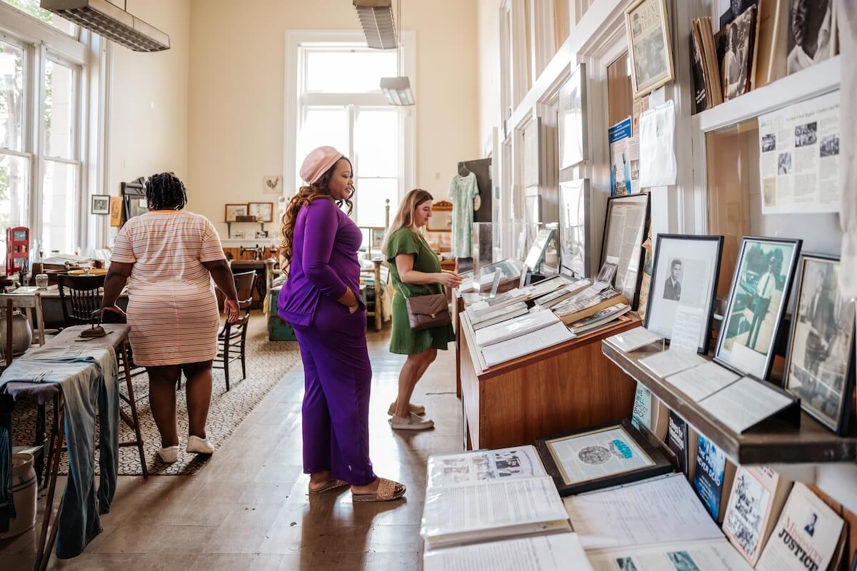 Why Natchez, MS, Belongs on Your Summer Travel List - 6 Three women explore displays of historical documents and photographs in a well-lit museum in Natchez MS—a must-see destination to add to your summer travel list.
