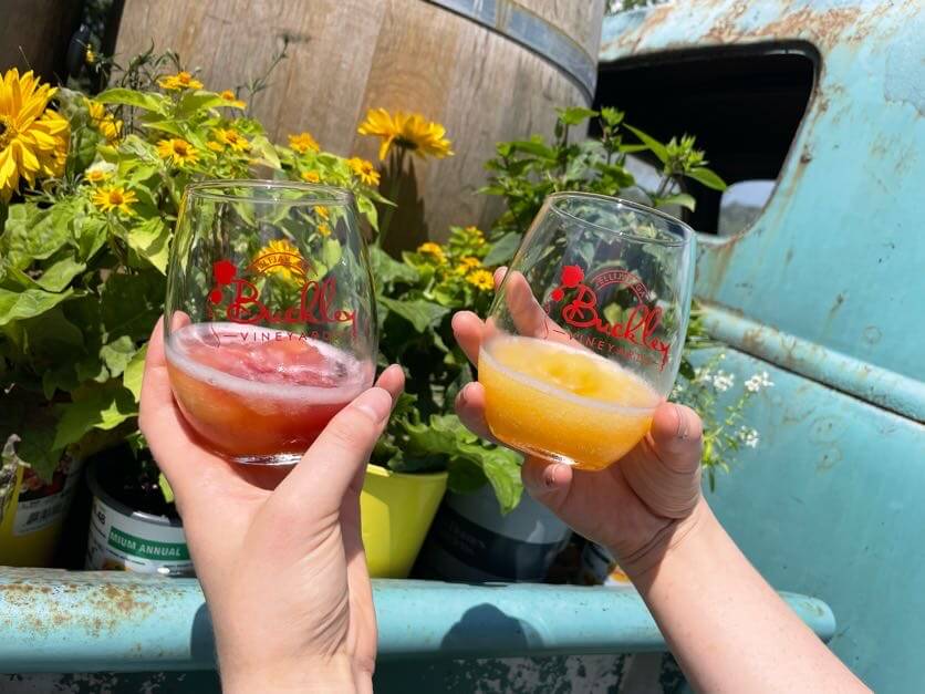 Georgia's 6 Best Girlfriends' Weekend Getaways - 8 Two hands clink wine glasses with colorful drinks in front of potted yellow flowers and a blue rustic vehicle.