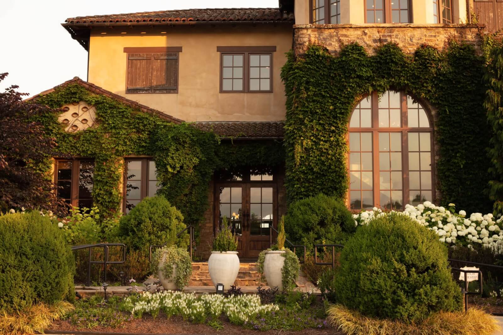 Georgia's 6 Best Girlfriends' Weekend Getaways - 7 A two-story house with ivy-covered walls, large windows, and a garden featuring bushes, flowers, and two large white planters by the entrance.