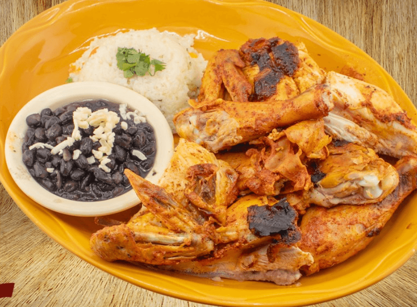 A plate with pieces of seasoned roast chicken, a serving of white rice garnished with cilantro, and a small bowl of black beans topped with cheese.