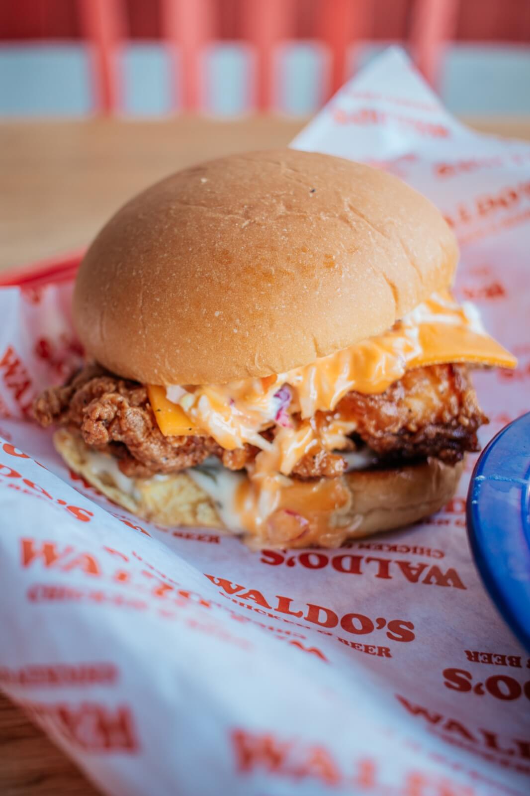 A fried chicken sandwich with cheese and sauce in a bun, served on branded paper.
