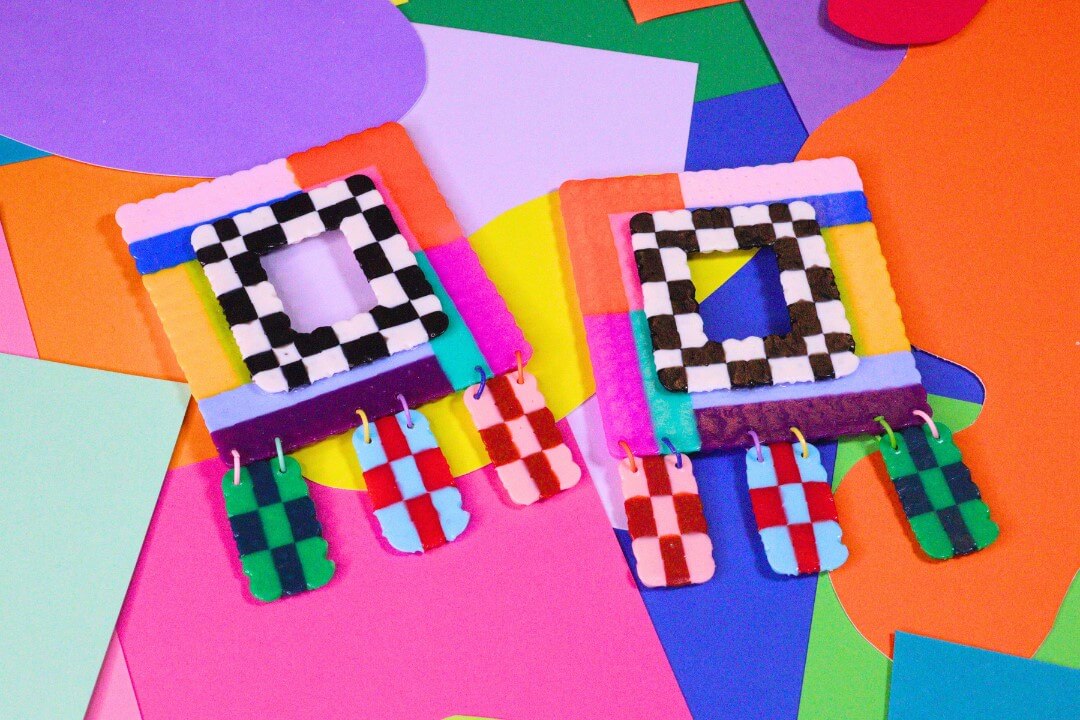 She's Behind BHAM's Most Colorful (and Secretly Nostalgic) Jewelry Line - 3 Two colorful, square-shaped earrings by jewelry designer Aaliyah Taylor, featuring checkerboard patterns and dangling rectangles, rest on multicolored paper shapes—exalting in beauty and bold artistry.