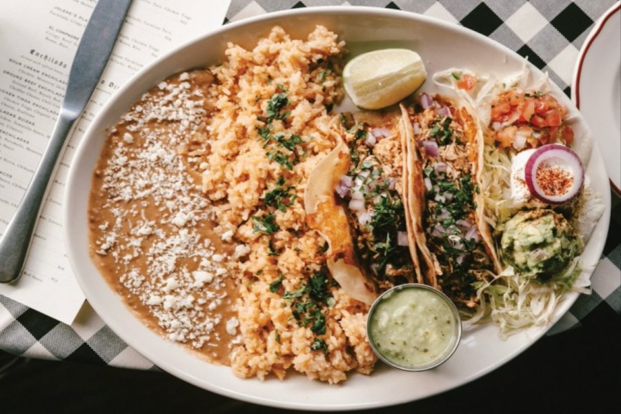 A plate with refried beans, Mexican rice, two tacos with cilantro and onion, a lime wedge, guacamole, salad, and green sauce on a checkered tablecloth—perfect for discovering flavors at new restaurants in Birmingham.