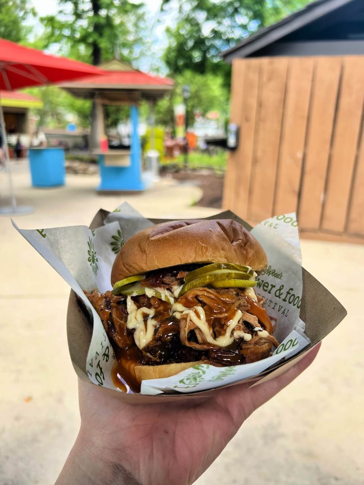 A hand holds a barbecue pulled pork sandwich with pickles and coleslaw in a paper tray at Dollywood.