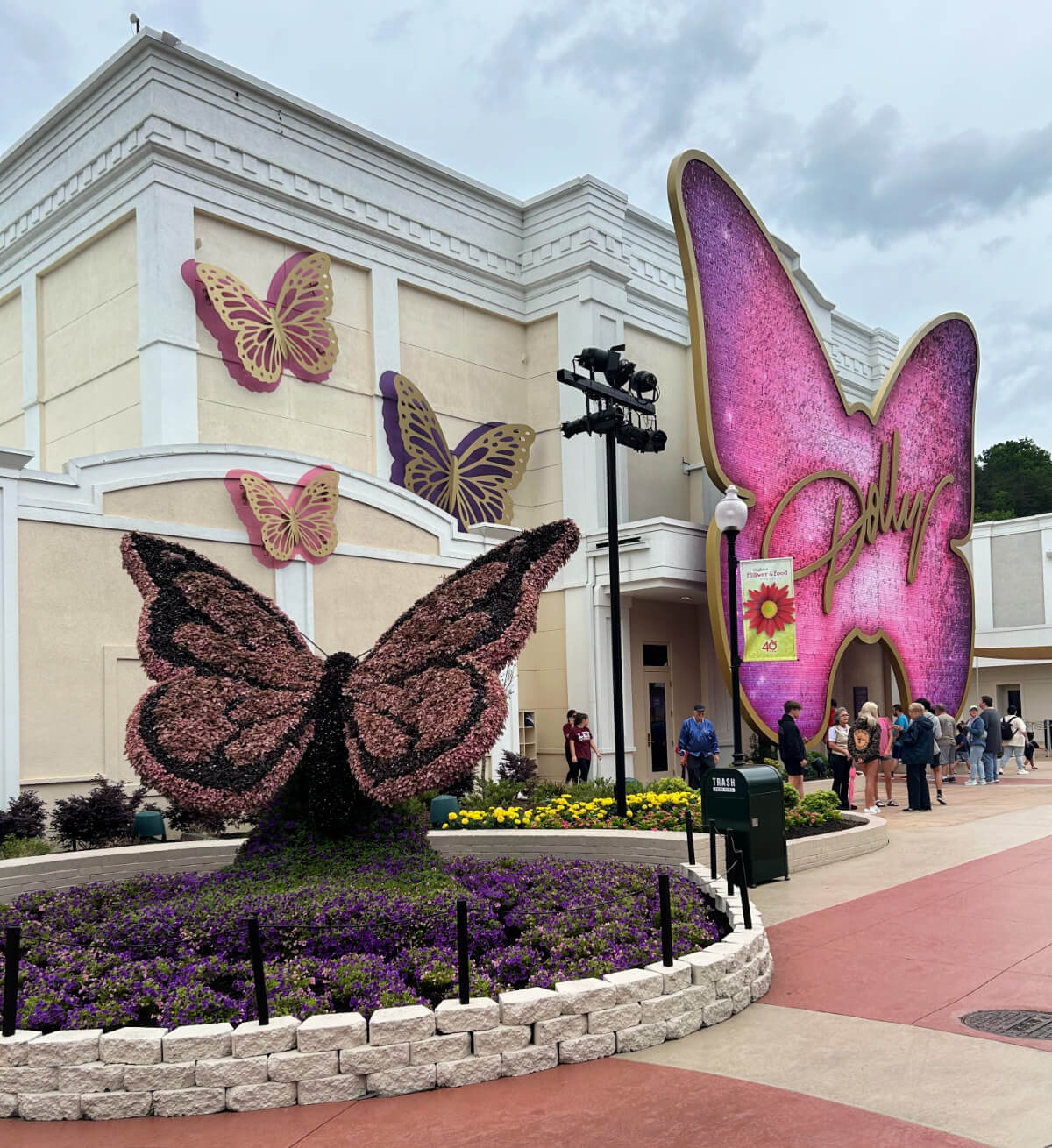 People stand outside a cream-colored building decorated with large pink butterfly sculptures and a "Dolly" sign in gold script, hinting at Dollywood-inspired charm and fun things to do nearby.