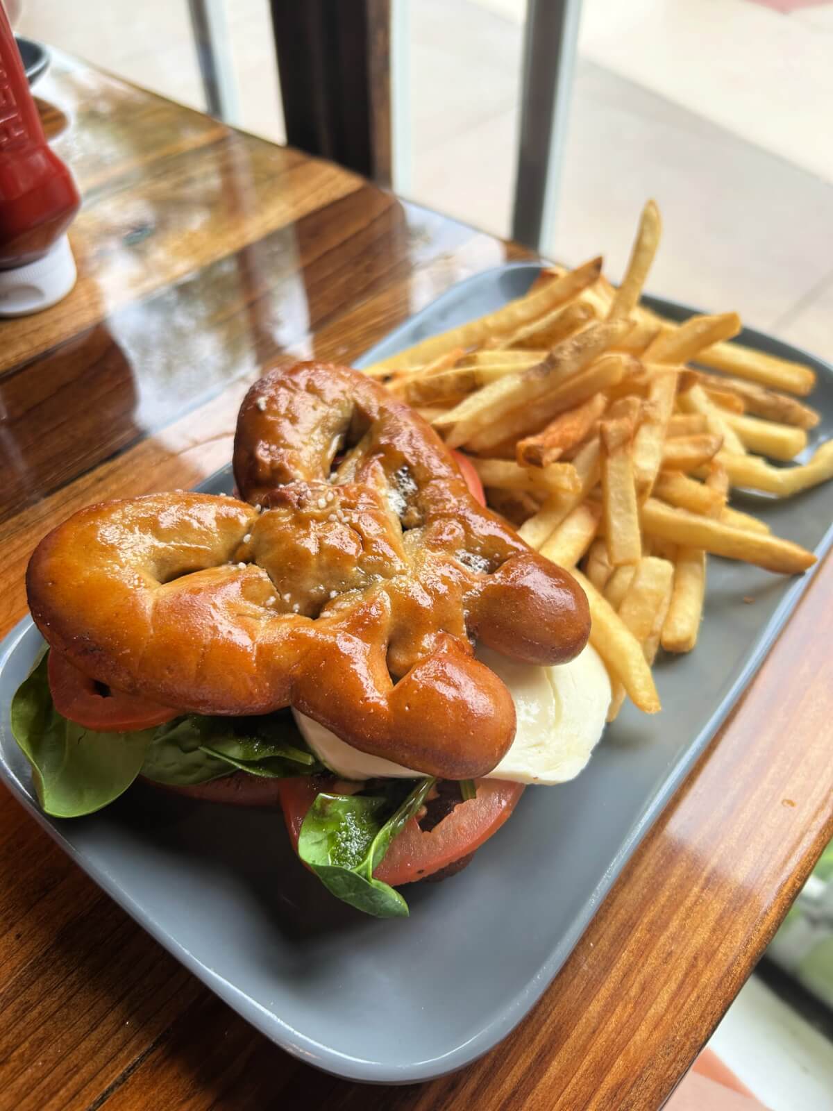 A sandwich with spinach, tomato, and mozzarella on a pretzel bun is served with French fries on a gray rectangular plate—perfect fuel for exploring Dollywood or other top attractions and things to do nearby.