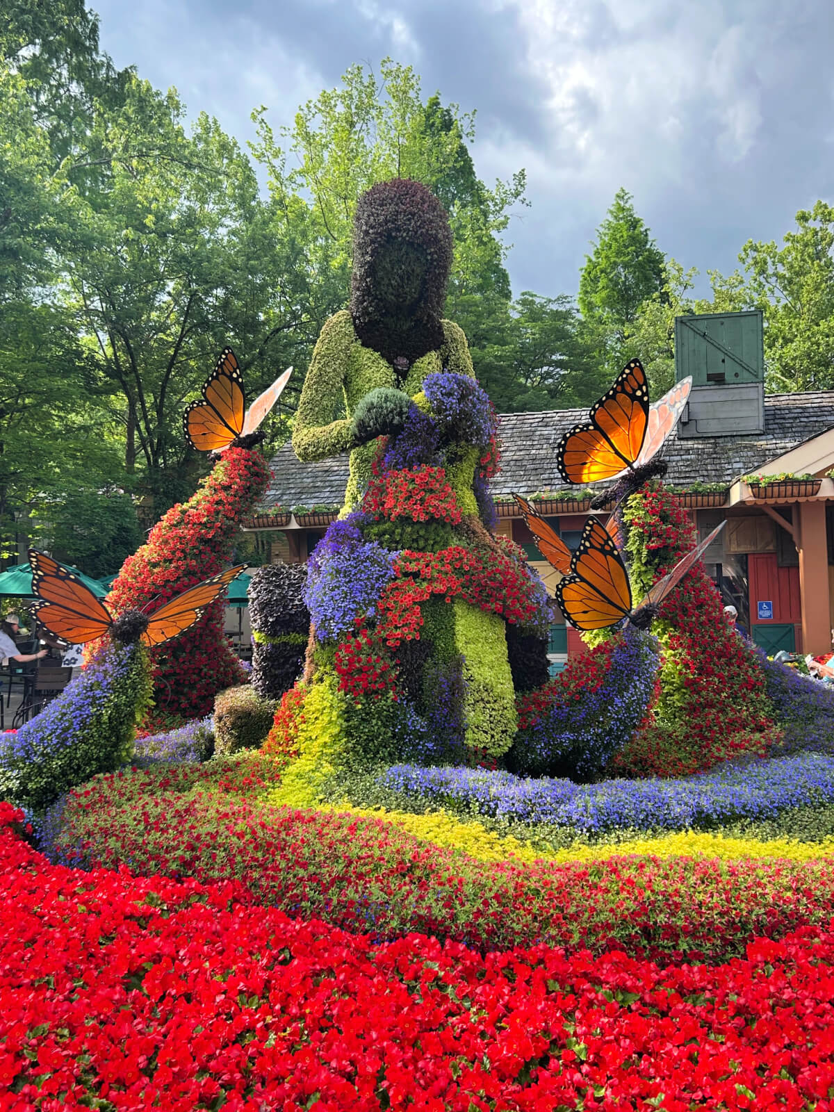 A large garden sculpture made of colorful flowers shaped like a person surrounded by butterflies, with trees and a building in the background—one of the unique things to do at Dollywood for nature and art lovers alike.