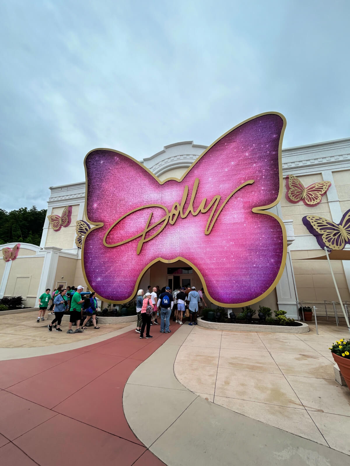 People walk toward a building entrance with a large, pink butterfly sign that reads "Dolly"—one of the unique attractions at Dollywood. Other butterfly decorations are visible on the building facade.