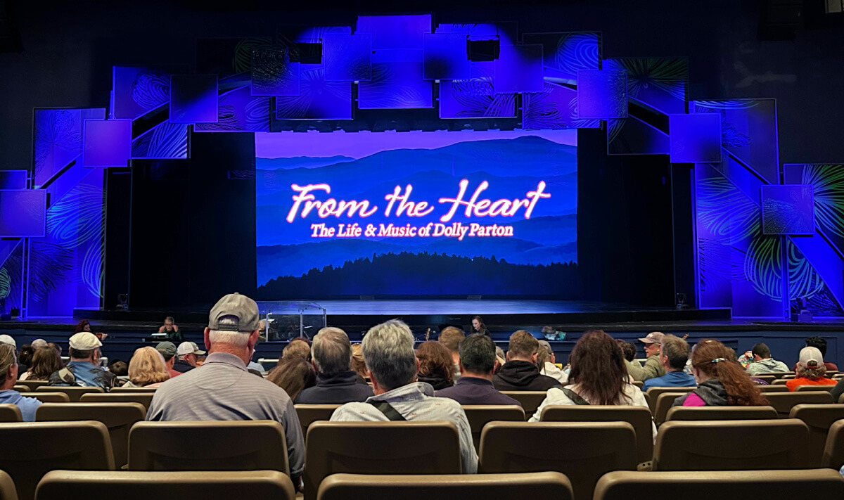 Audience seated in a theater at Dollywood, one of the top attractions, facing a stage with a large screen displaying "From the Heart: The Life & Music of Dolly Parton" against a blue and purple backdrop—an unmissable addition to your list of things to do.