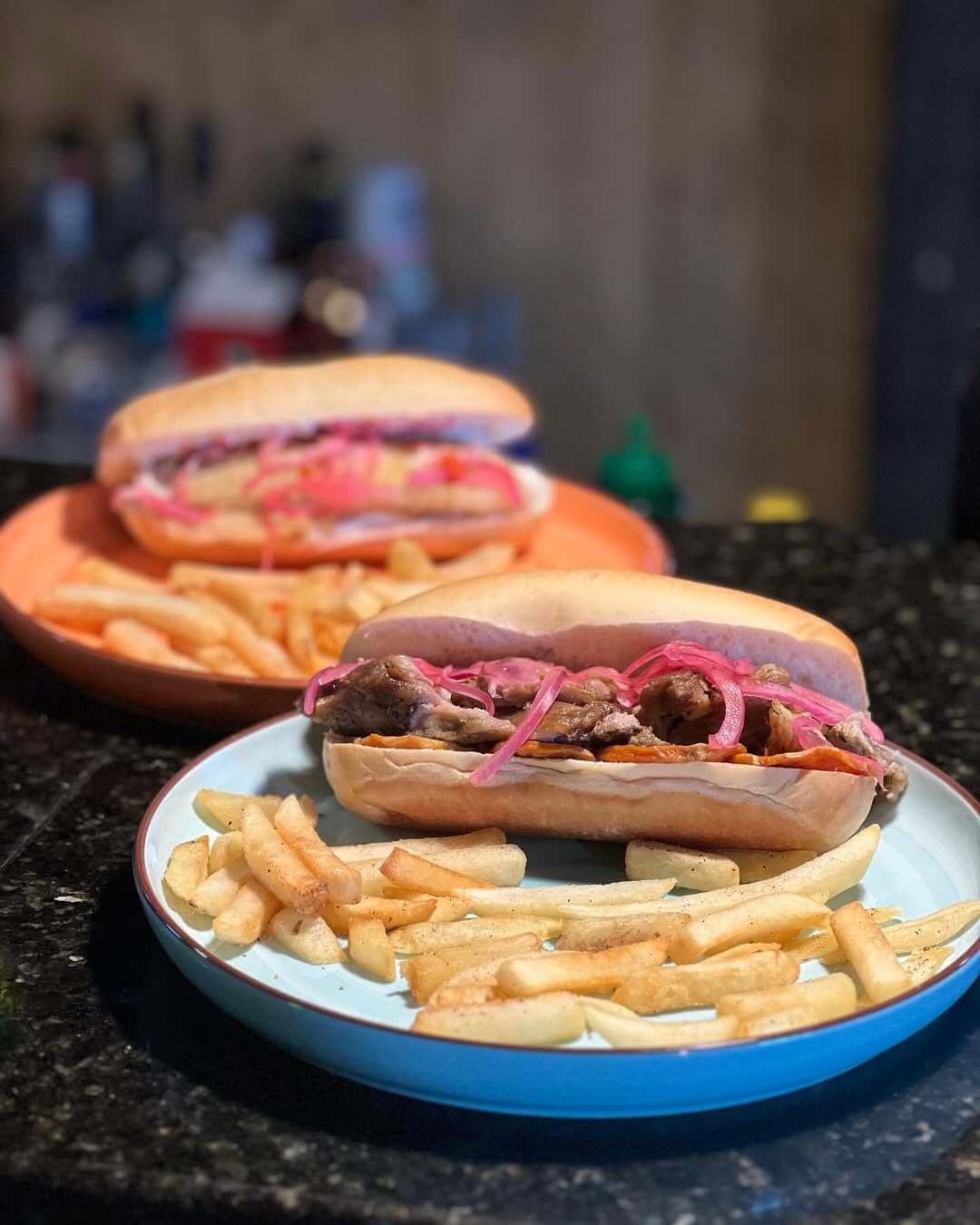 Two plates with sandwiches filled with meat and pickled onions, each served with a side of French fries—a must-try from the new menu at standout Louisville restaurants.