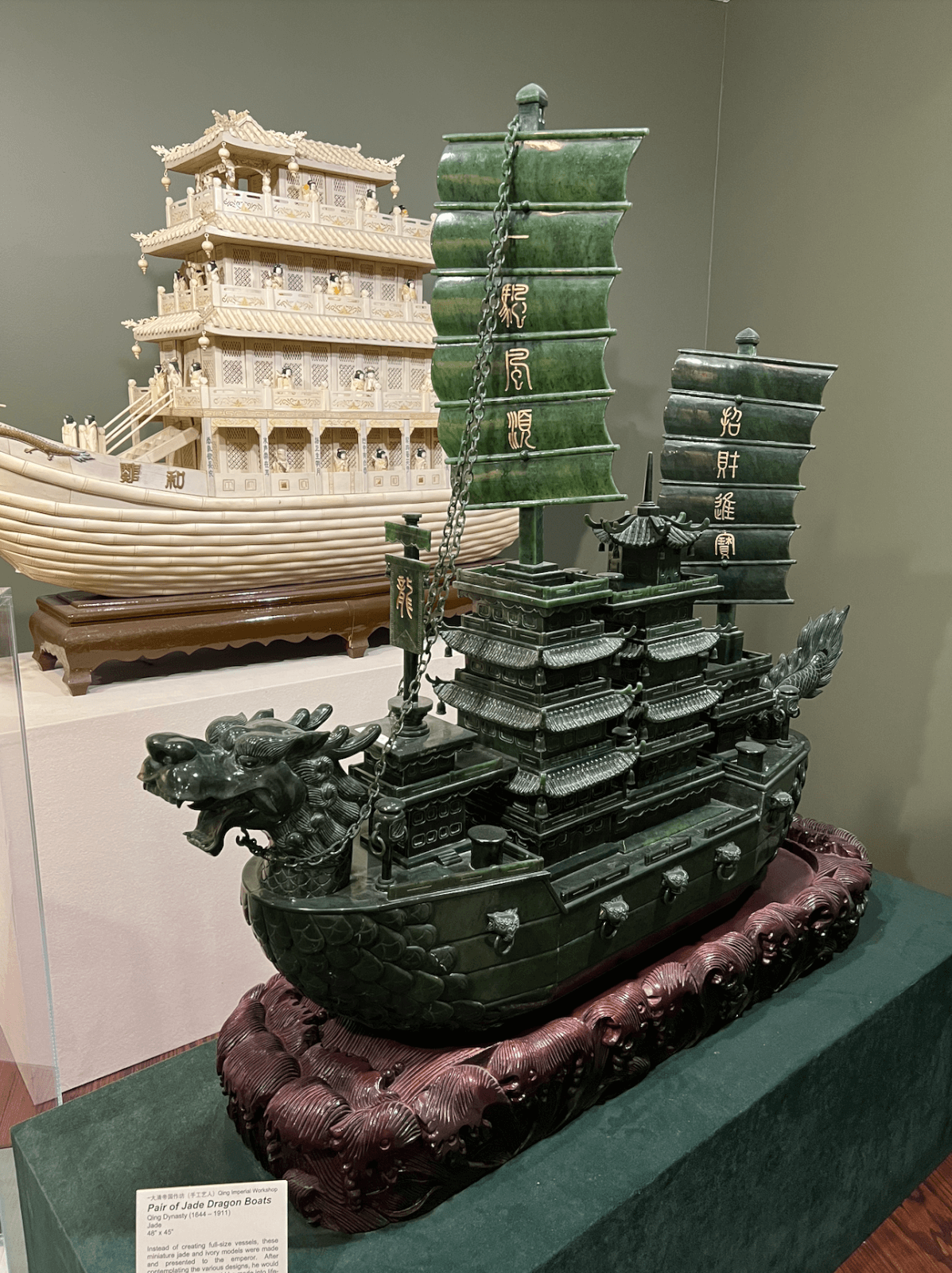 A detailed jade sculpture of a dragon boat with Chinese sails is displayed on a maroon base at the Belz Museum, one of Memphis’s best-kept secrets, with another ornate model boat showcased in the background.