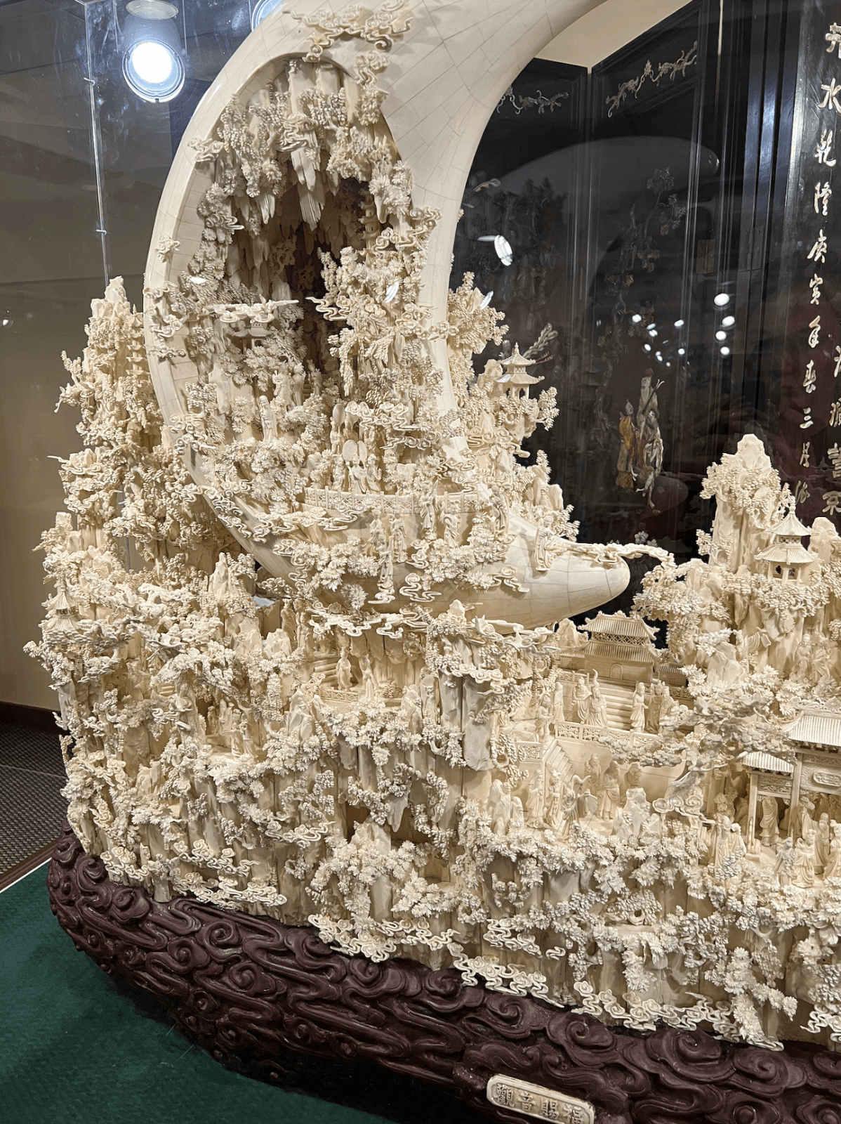 Intricately carved ivory sculpture featuring numerous small human figures amid detailed structures, with a large crescent shape at the top, displayed in a museum case at the Belz Museum, Memphis’s best-kept secret.