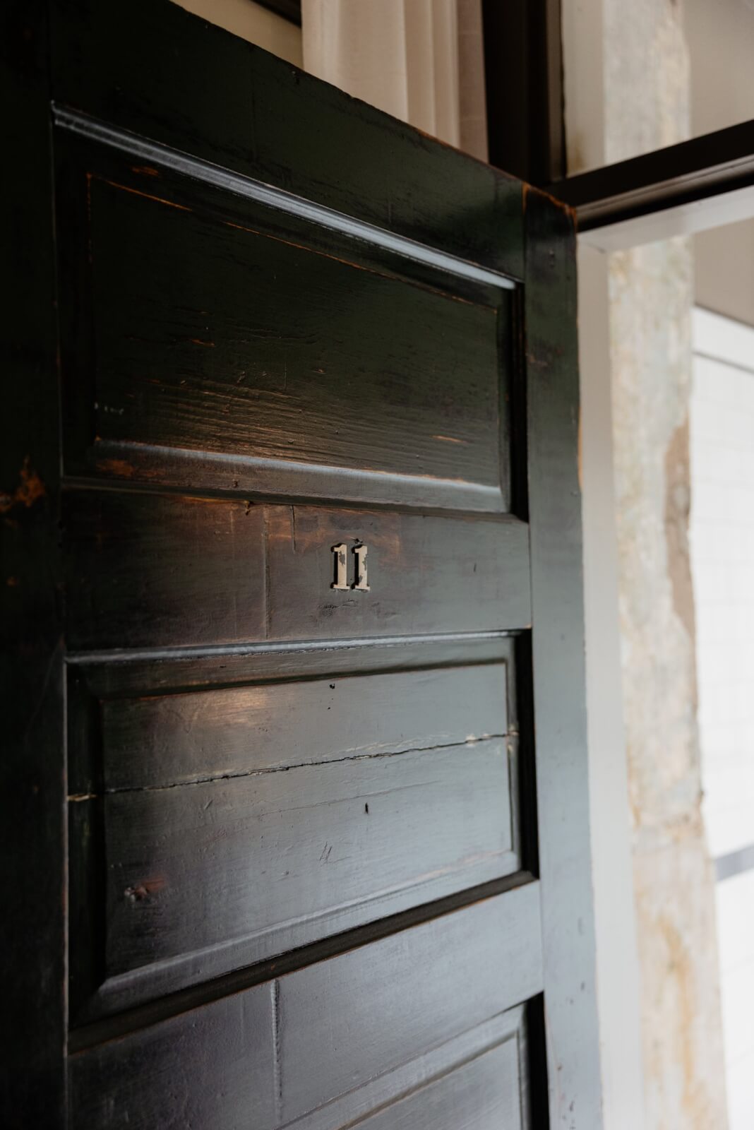 A dark green wooden door with the number 11 is slightly open, revealing part of a light-colored wall and window frame in the background of this vintage hotel in Memphis.