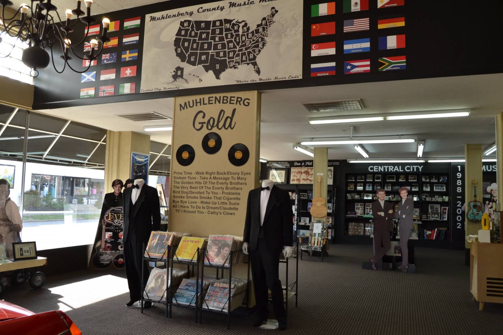 Interior of a music museum in Western Kentucky featuring records, album displays, mannequin figures in tuxedos, and a wall map of the United States with flags and music-themed decor.