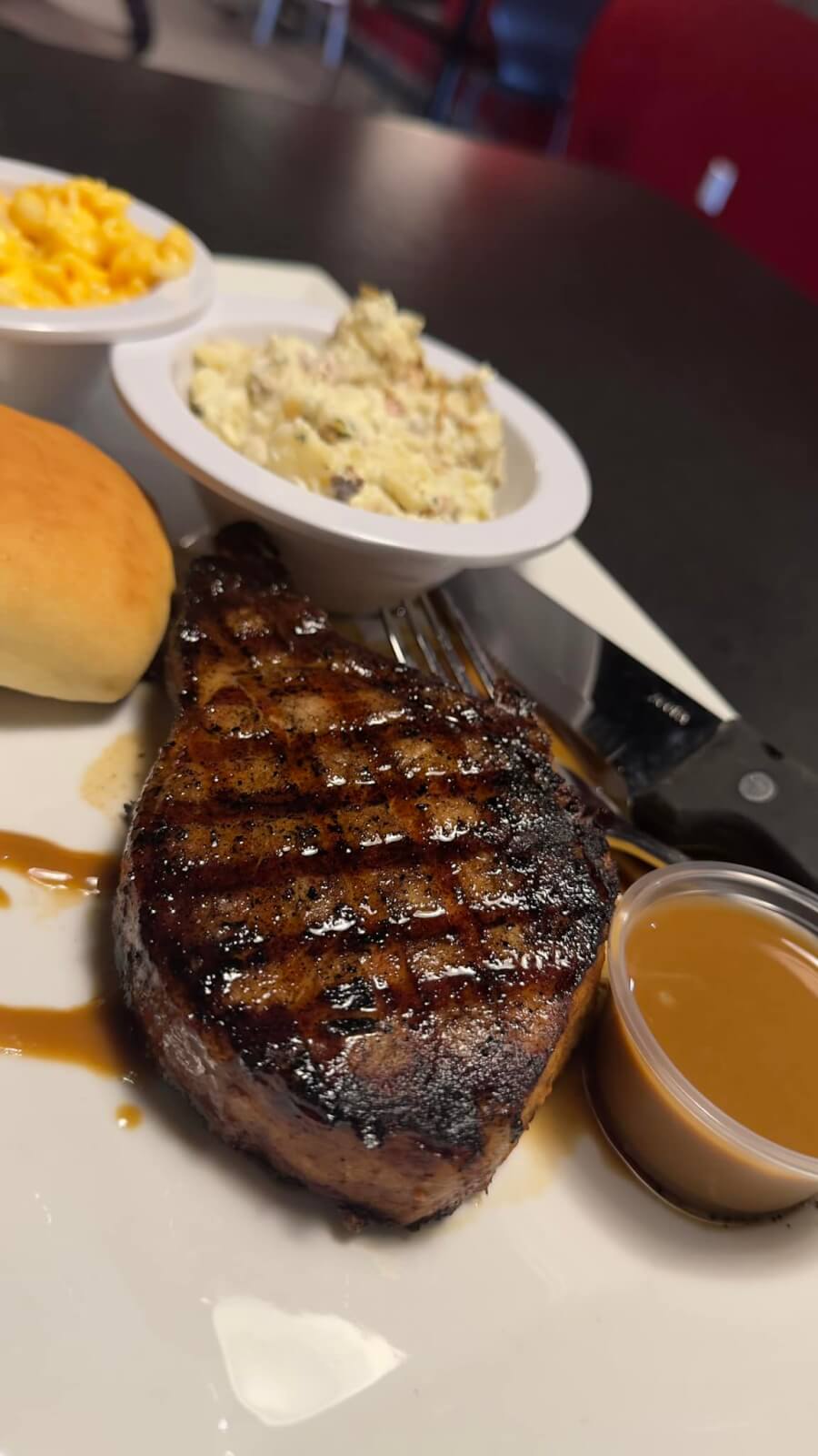 A grilled steak with sauce on the side, served with a dinner roll, macaroni and cheese, and a bowl of potato salad—classic Western Kentucky comfort for those seeking Big Experiences in Small Towns.
