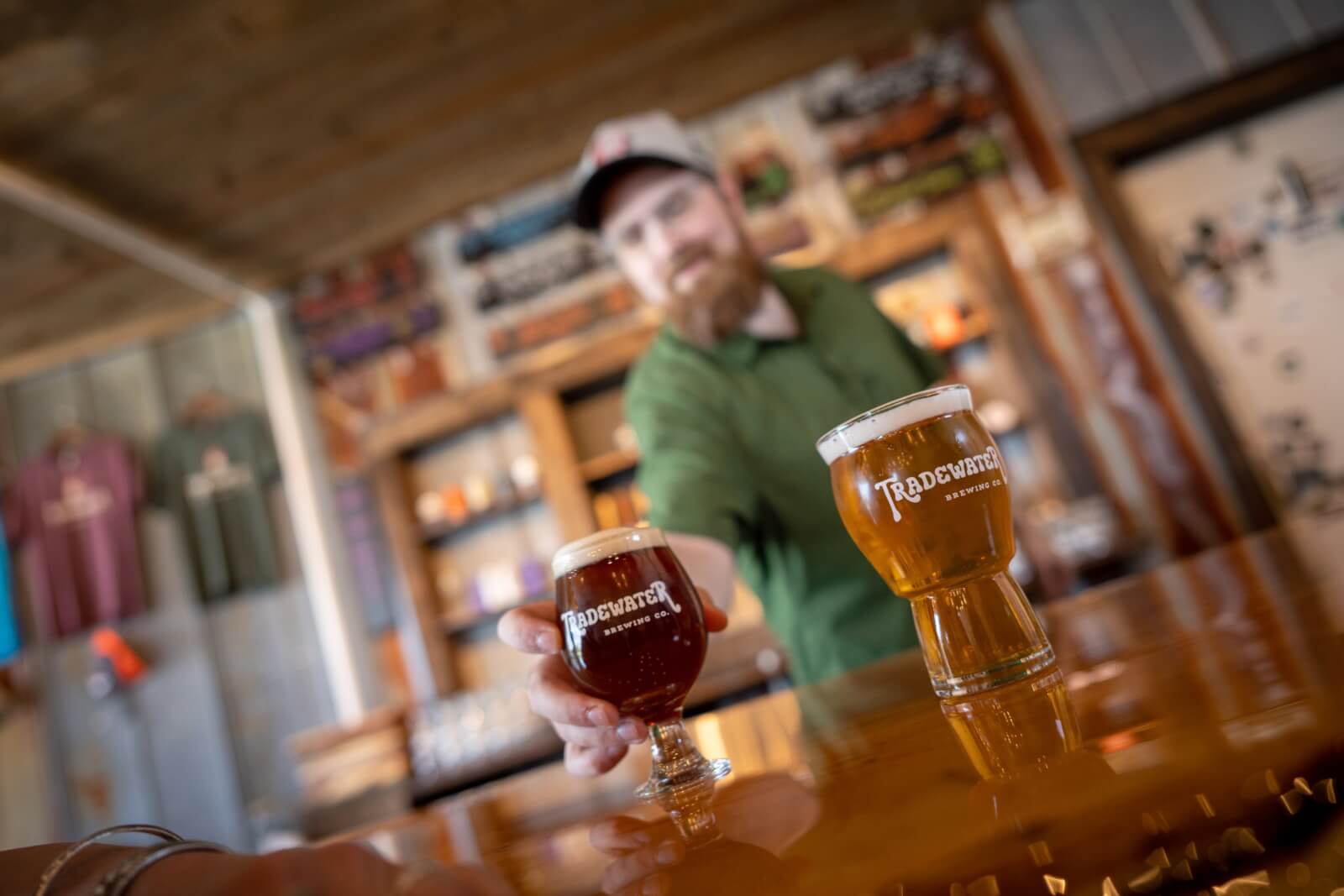 A bartender places a glass of dark beer on the bar next to a pale ale, both branded with the Tradewater Brewing Company logo—a proud taste of Western Kentucky’s small towns.