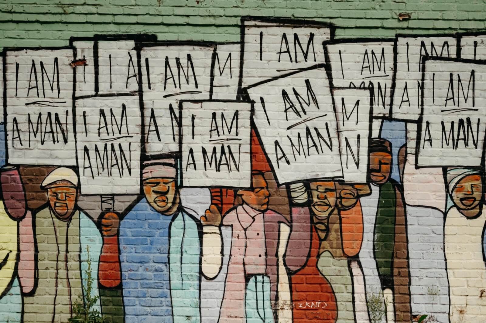 Mural exploration reveals a powerful scene: a group of people holding "I AM A MAN" signs against a brick wall, highlighting the impact of Memphis street art.