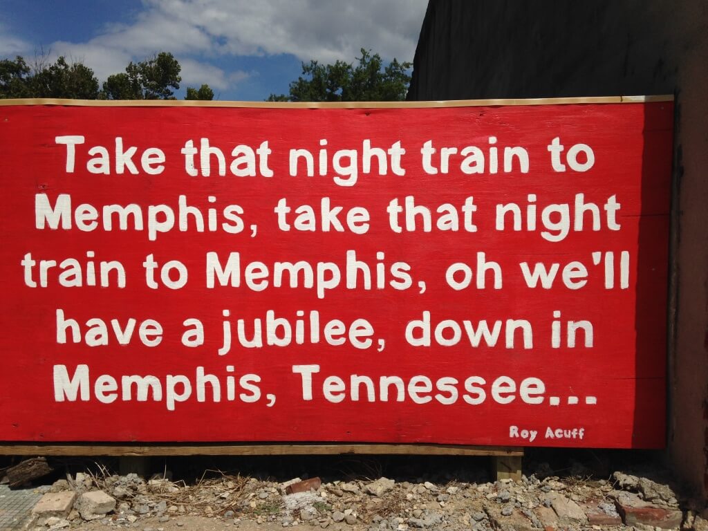 Red sign with white text quoting song lyrics about taking a night train to Memphis, Tennessee, attributed to Roy Acuff—a vibrant piece for those on a Memphis Murals or mural exploration journey.