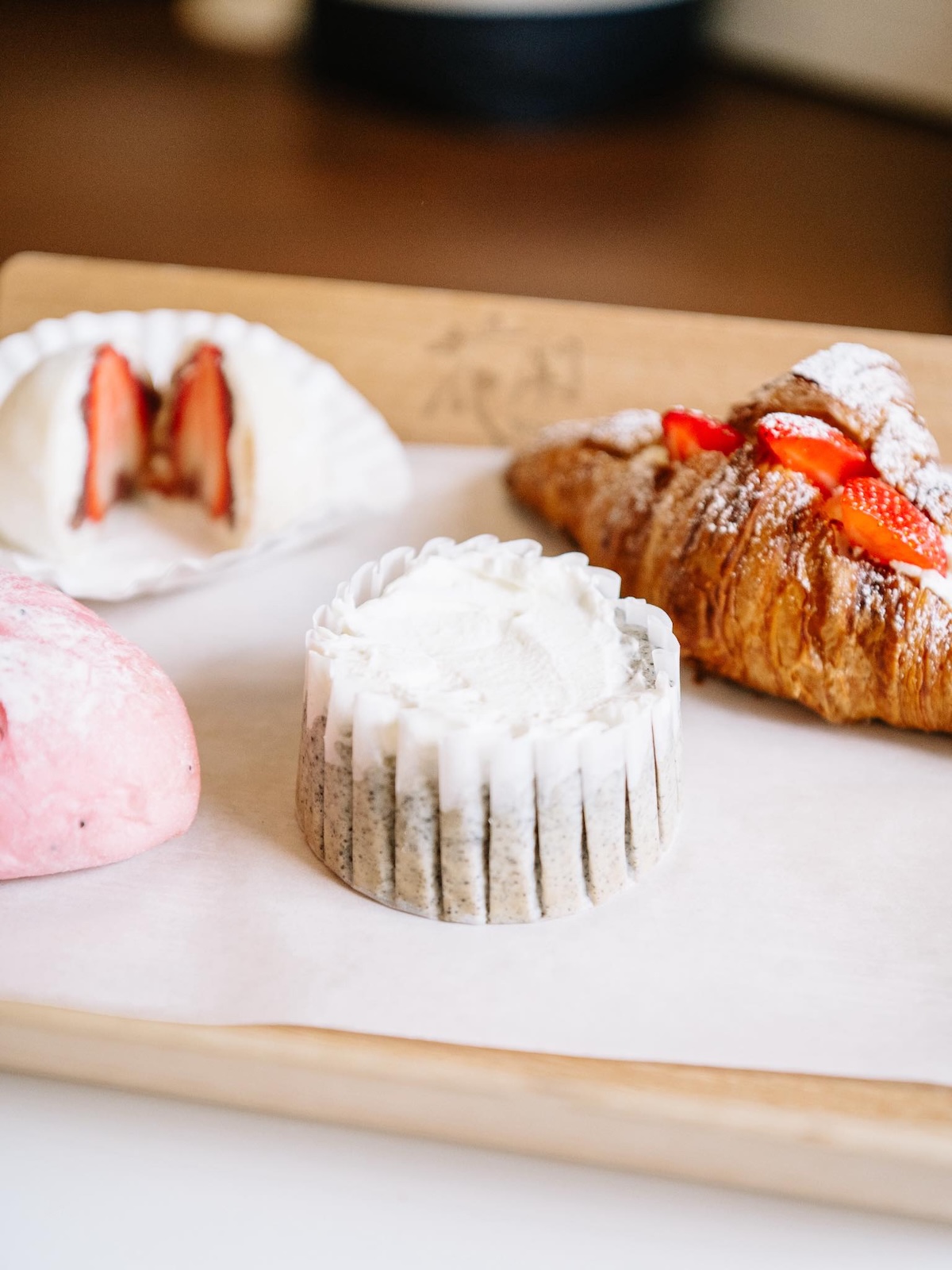 A tray with assorted pastries, including a croissant topped with strawberries, a round pastry with white cream, and two pink pastries—one cut to show a strawberry filling.