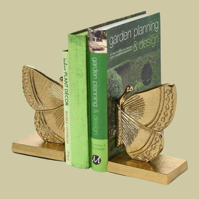 20 Spring FINDS for Mother’s Day & Beyond: Style, Beauty & Home Must-Haves - 14 Two gold butterfly-shaped bookends hold three gardening books upright against a light green background, perfect for adding charm to shelves found in curated Nashville shops.