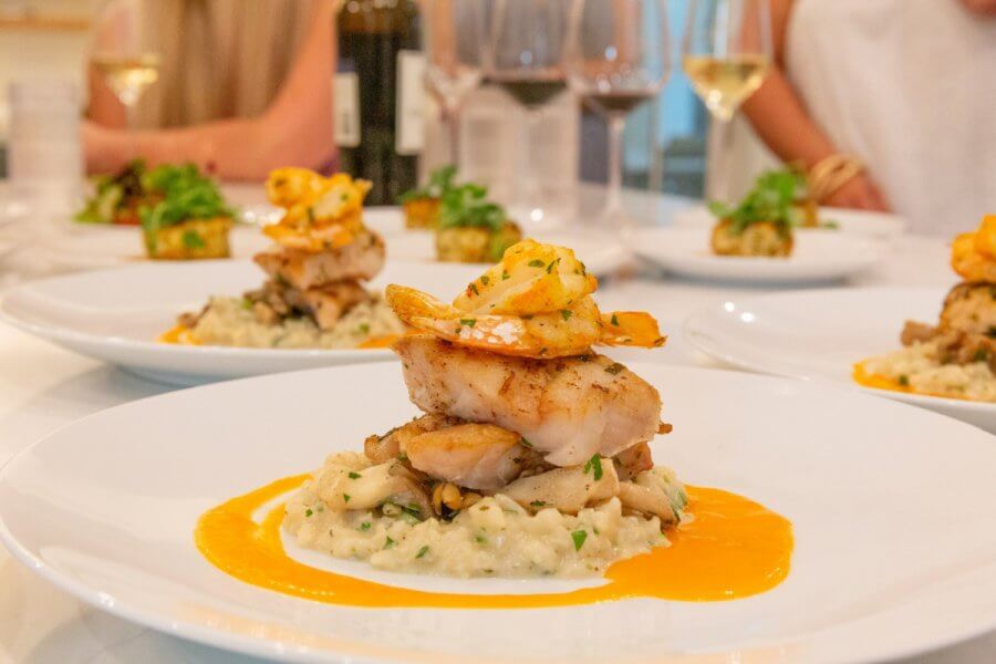 5 Reasons South Walton is Becoming the Premier Destination for Corporate Events and Meetings - 11 A plated dish featuring grilled fish and shrimp on a bed of risotto with a creamy orange sauce, served at a table with wine glasses—perfect for event hosting at South Walton's premier venues.