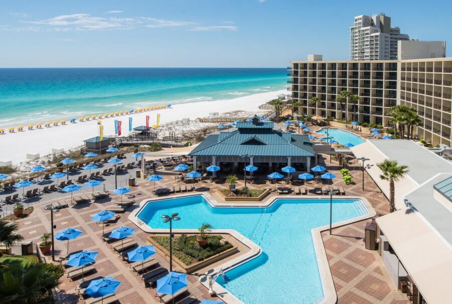 5 Reasons South Walton is Becoming the Premier Destination for Corporate Events and Meetings - 4 A beachfront resort features a large outdoor pool area with blue umbrellas, lounge chairs, and direct access to a white sandy beach and turquoise ocean—perfect for your next event in South Walton.