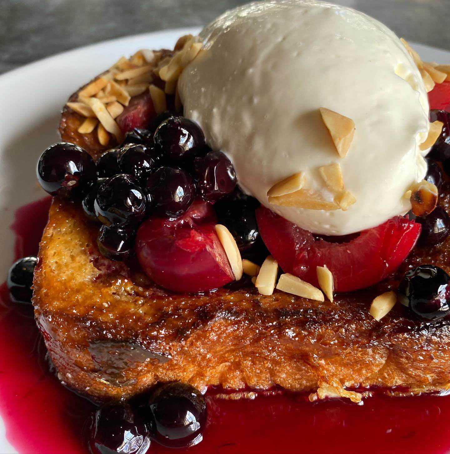 A thick slice of French toast topped with vanilla ice cream, blueberries, cherries, slivered almonds, and fruit syrup—perfect for a Mother's Day brunch in Birmingham.