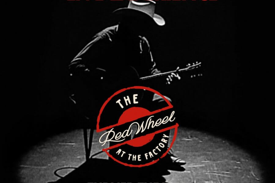 A person in a cowboy hat sits on a chair playing an acoustic guitar in a dark, spotlighted room with "The Red Wheel at The Factory" logo overlayed, capturing the essence of the Songwriter Series.