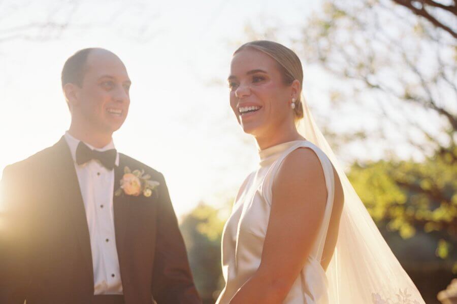 Nashville’s 10 Most Popular Articles of 2025 - 8 A bride in a white dress and veil stands next to a groom in a tuxedo, both smiling outdoors with sunlight in the background at their beautiful Cheekwood wedding in Nashville.