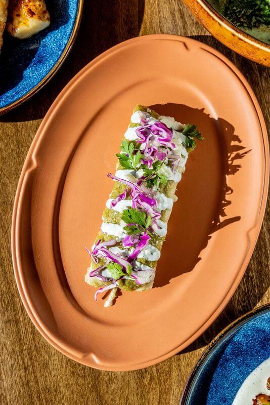 9 New Nashville Restaurants to Try This Month - 15 A rectangular piece of food topped with white sauce, purple cabbage, and green herbs is served on an oval terracotta plate—a delightful find at new Nashville restaurants opening in May 2025.