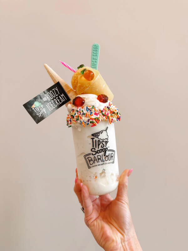 9 New Nashville Restaurants to Try This Month - 16 A hand holding a plastic shake cup filled with ice cream and toppings, with a flag that reads "#boozyicecream."