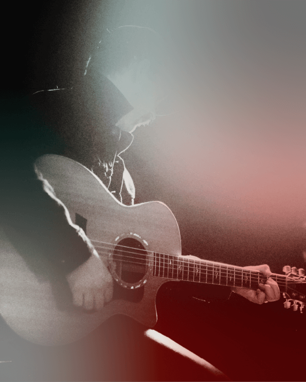 A person in a hat and jacket is playing an acoustic guitar under low lighting, with a red and gray filter overlay.