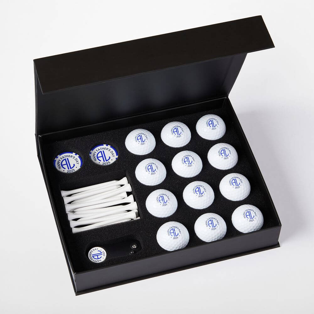 A perfect pick for golf gifts, this black box features twelve white golf balls, ten tees, a ball marker, and a divot tool—each with a blue circular logo—neatly arranged in foam. Ideal for any gift guide or Father’s Day gifts.