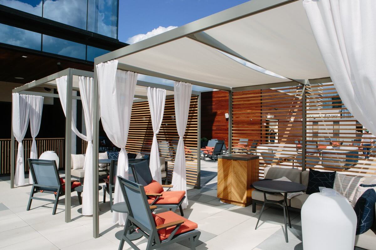 Outdoor patio area with shaded cabanas, white curtains, lounge chairs with orange cushions, and wooden slat dividers—perfect for relaxing after a day at CMA Fest under a clear sky.