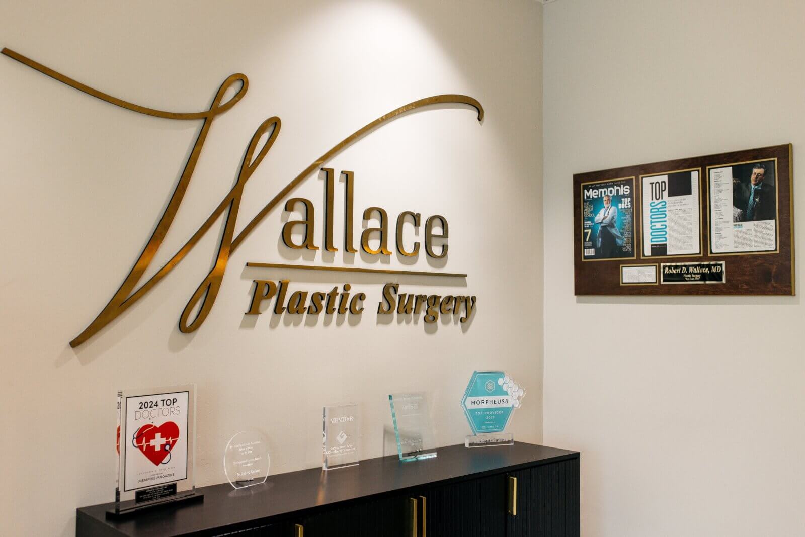 The Wallace Plastic Surgery office in Memphis features a gold sign, framed awards, plaques, and certificates on a black cabinet—reflecting its recognition among Top Plastic Surgeons.