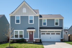 Charming two-story gray house with white trim at 513 Red Hill Ct, Brentwood TN, featuring a red front door with a wreath, attached double garage, and a small front lawn under a clear blue sky—perfect real estate opportunity.