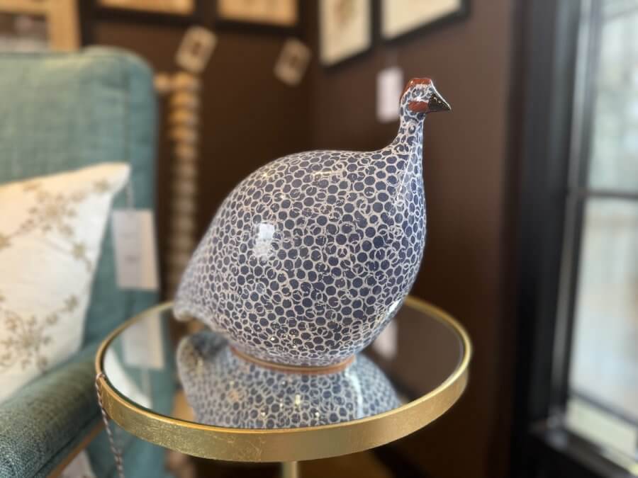 A ceramic bird figurine with a blue and white dotted pattern sits on a round glass-top table next to a green upholstered chair, adding unique home decor style inspired by a Nashville home store.