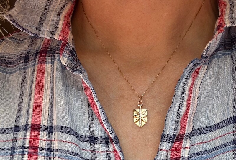 A person wearing a plaid shirt and a gold shield-shaped pendant necklace, showcasing relaxed summer essentials.