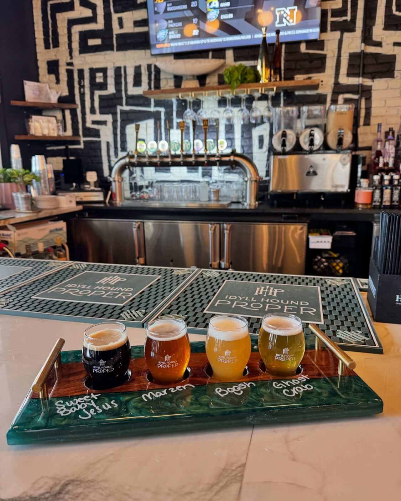 A flight of four beers is arranged on a tray atop a bar counter along scenic 30A, with bar taps and glassware visible in the background.